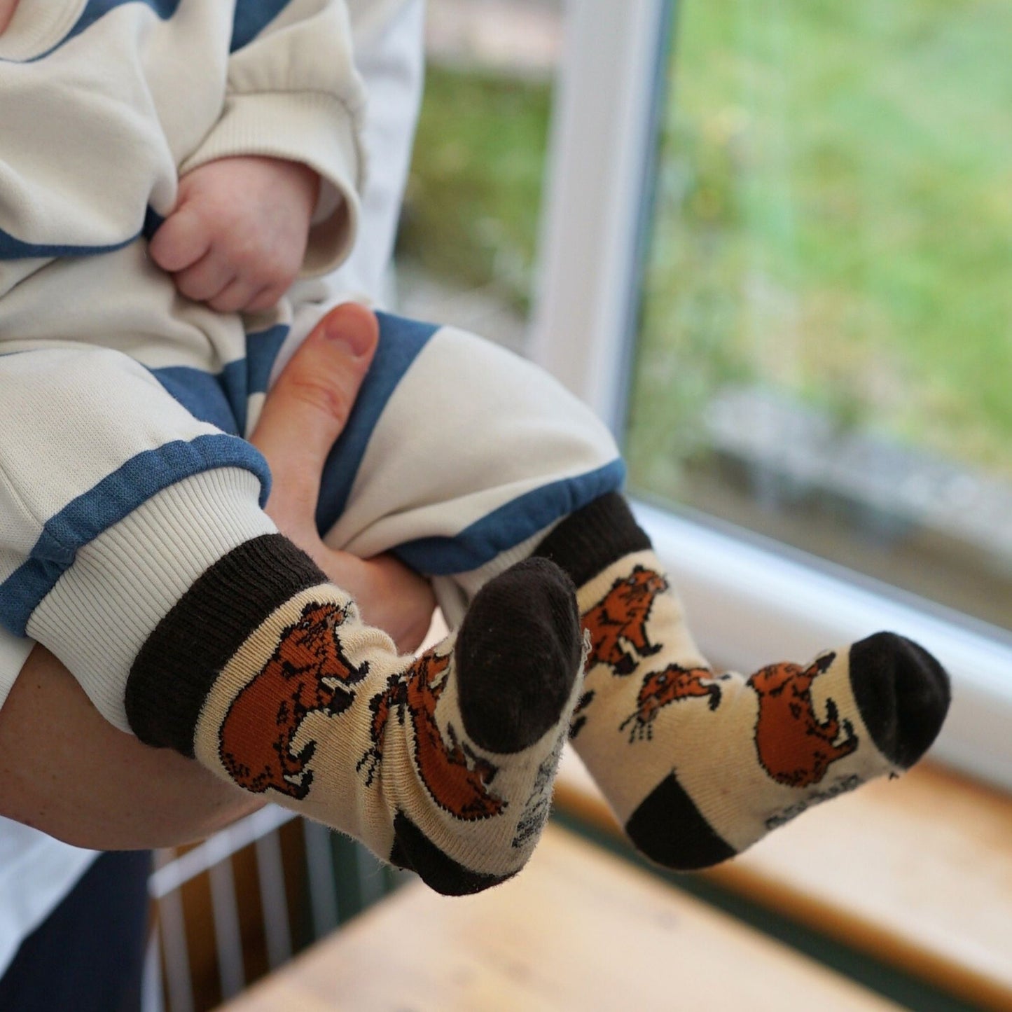Baby's feet wearing socks with capybara designs, held by an adult.