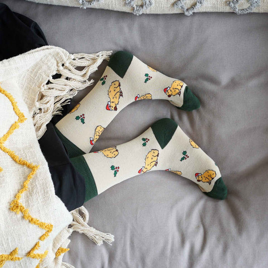 Pair of capybara socks on a gray surface next to a white blanket with yellow patterns.