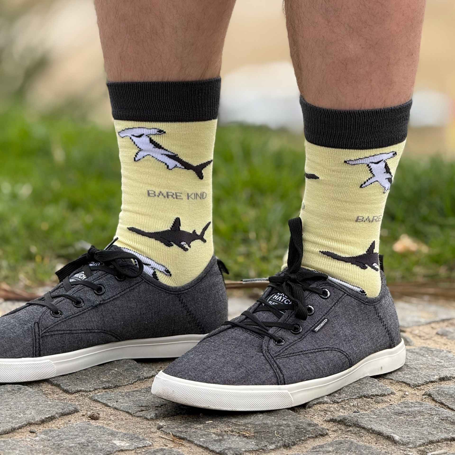 Person wearing socks with shark design and 'Bare Kind' branding outdoors.