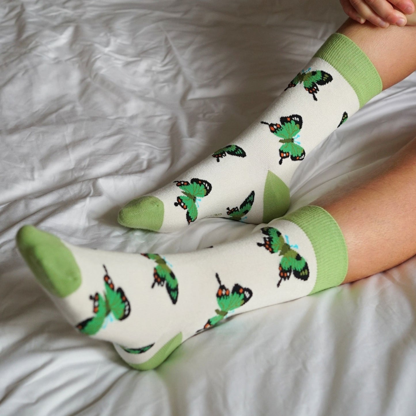 Person wearing socks with green and black designs on a white bed.