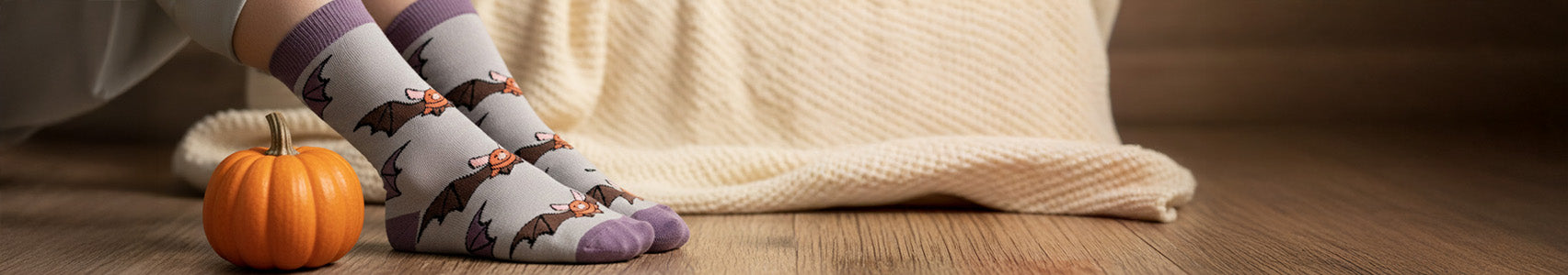 Person wearing bat socks with a small pumpkin on a wooden floor.