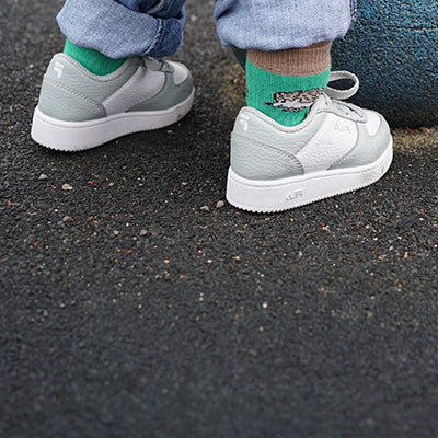 Kid wearing light gray sneakers and green hedgehog socks with a design on a dark surface