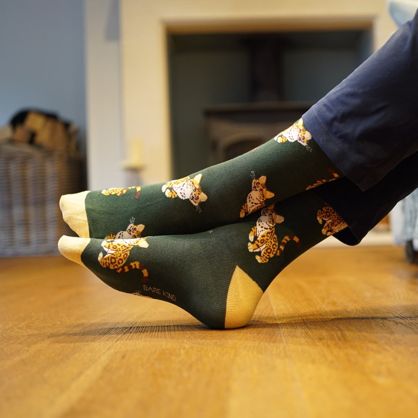 Green socks with leopard cat pattern worn by a person sitting on a wooden floor.