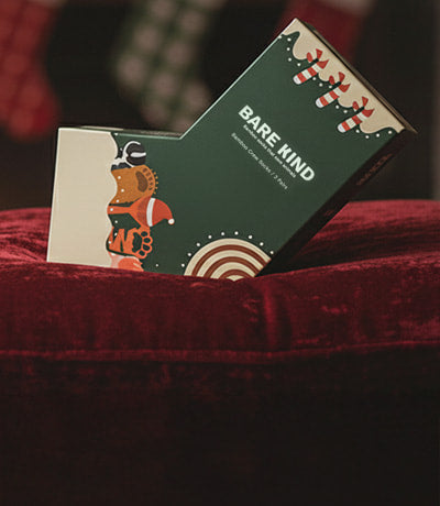 Bare Kind christmas gift box on a red surface in front of a fireplace with Christmas decorations.