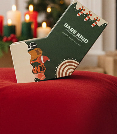 Bare Kind christmas gift box on a red surface in front of a fireplace with Christmas decorations.