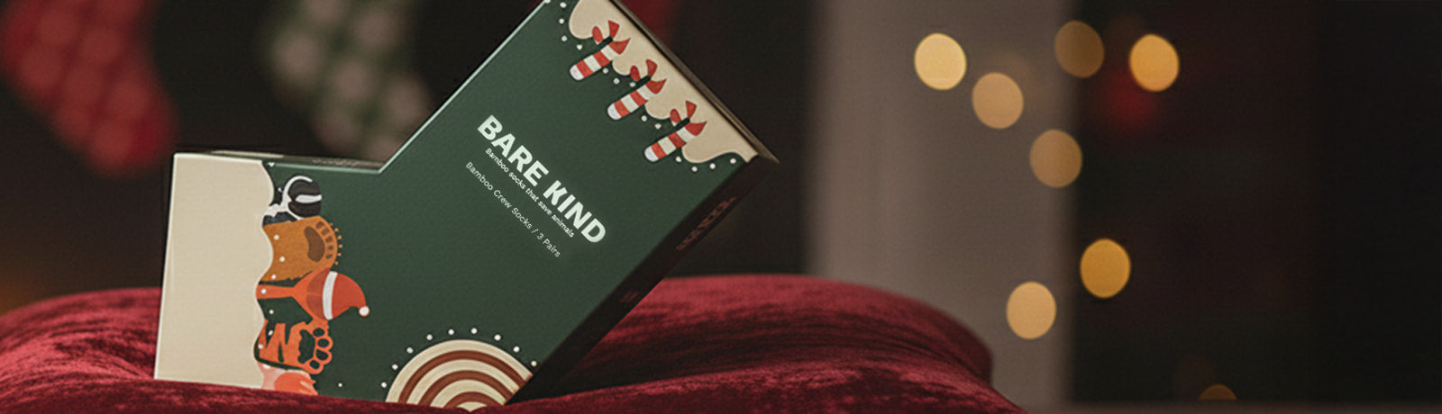 Bare Kind christmas gift box on a red surface in front of a fireplace with Christmas decorations.