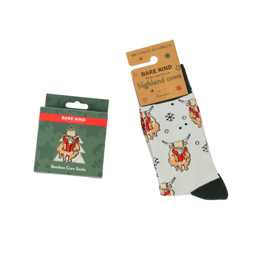 Bare Kind bamboo crew socks with a Highland cow print, shown both in their green retail packaging and hanging from a cardboard hanger.
