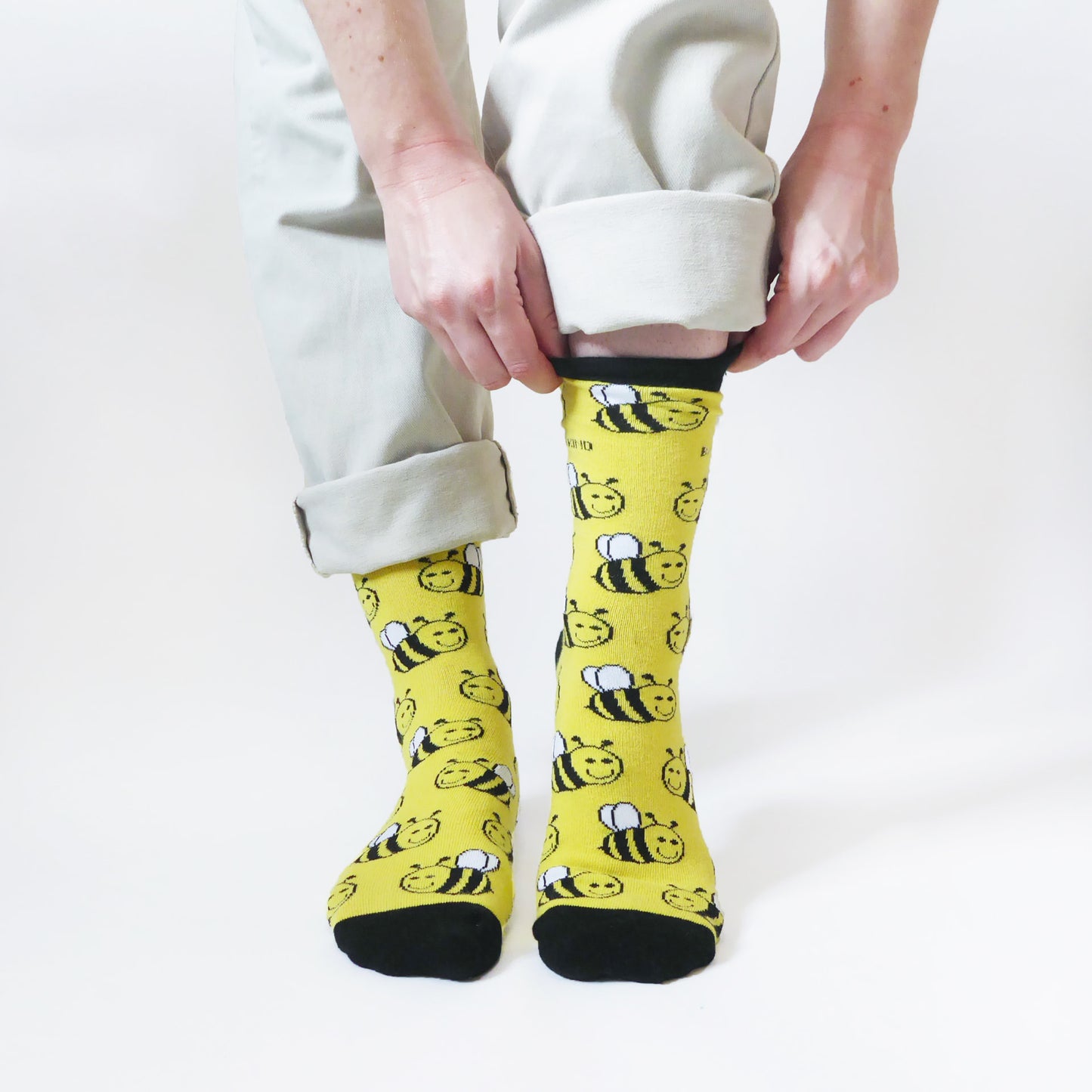 model stands and pulls up the left cuff of black and yellow bamboo bee socks