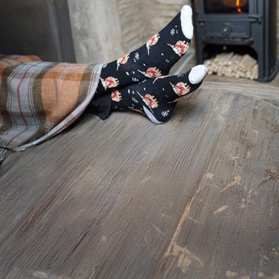 Person wearing highland cow socks on a wooden floor with a fireplace in the background