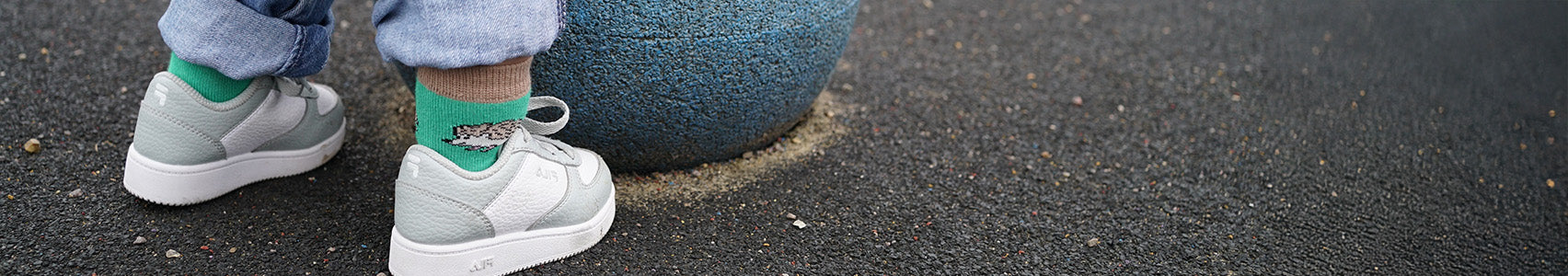 Kid wearing light gray sneakers and green socks with a blue ball on a dark surface