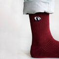 closeup of standing model wearing ruby red ribbed bamboo socks, showcasing embroidered panda motif on the cuff