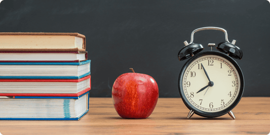 Books, an alarm clock, and an apple on a desk.