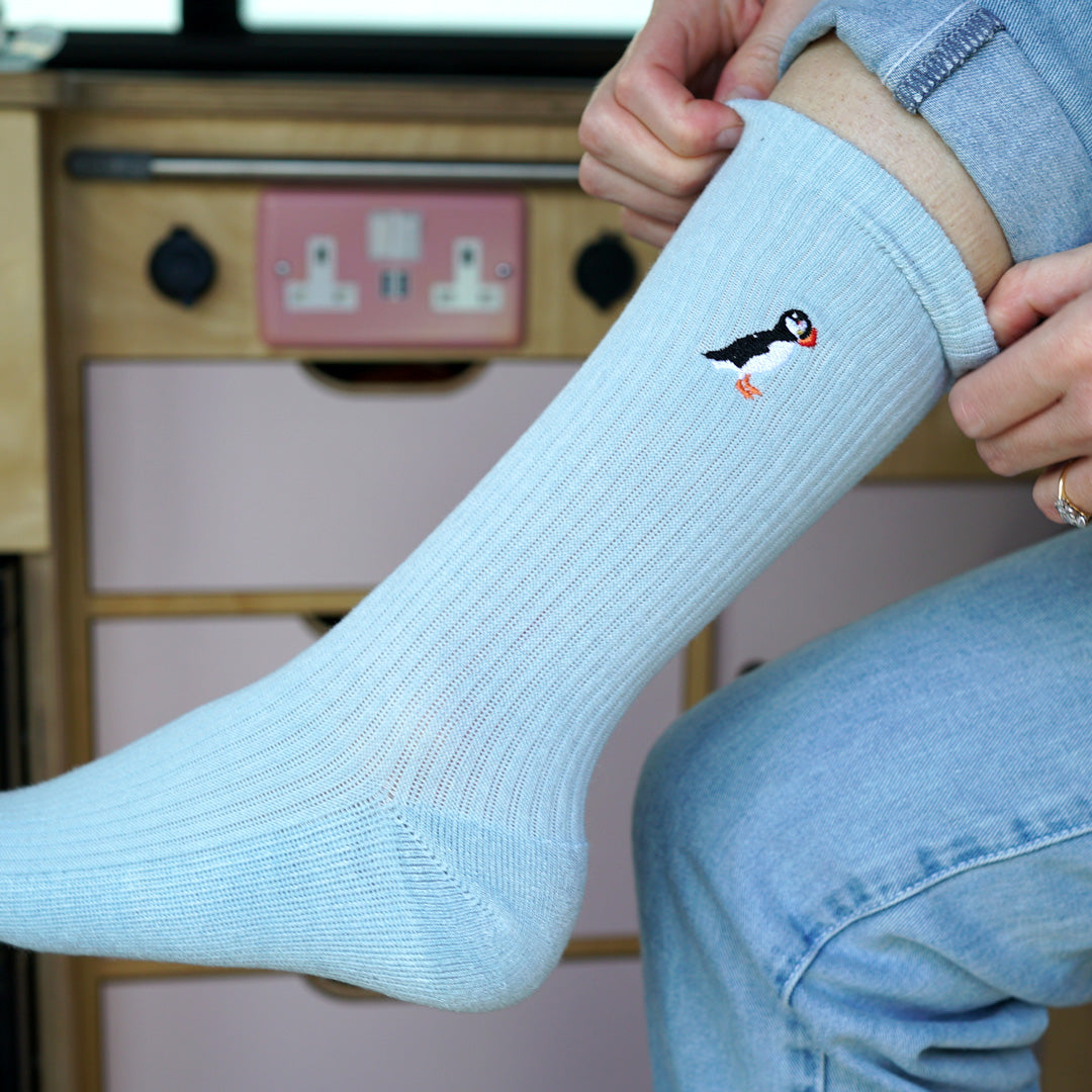 Model wearing blue ribbed pastel socks with puffin motif embroidered on cuff