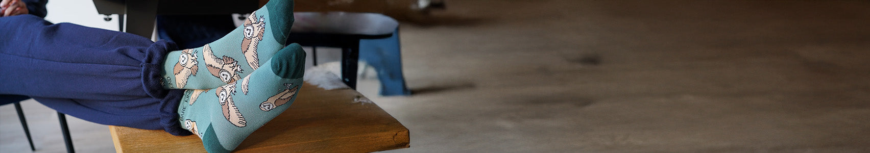 Barn owl socks worn by a person sitting on a wooden stool.