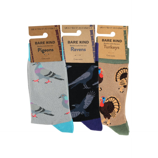 Three pairs of Bare Kind brand crew socks displayed side-by-side on their cardboard hangers against a white background. The left pair is light gray with a pigeon pattern and turquoise toes; the middle pair is black with a raven pattern and dark blue toes; the right pair is tan with a turkey pattern and green toes.