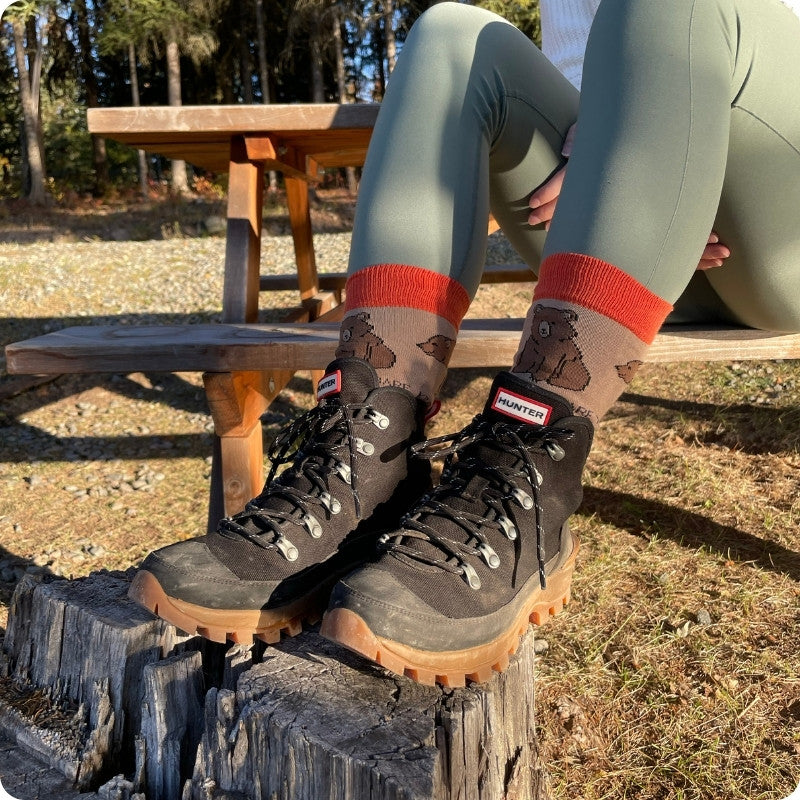 Person wearing Hunter boots and socks with bear design, sitting on a log outdoors.