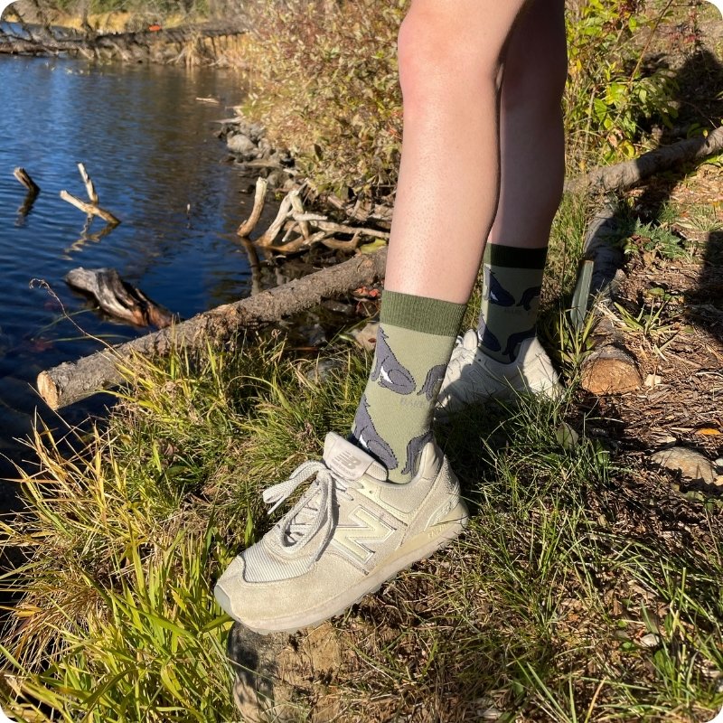 Person wearing green wolf socks and white sneakers by a body of water.