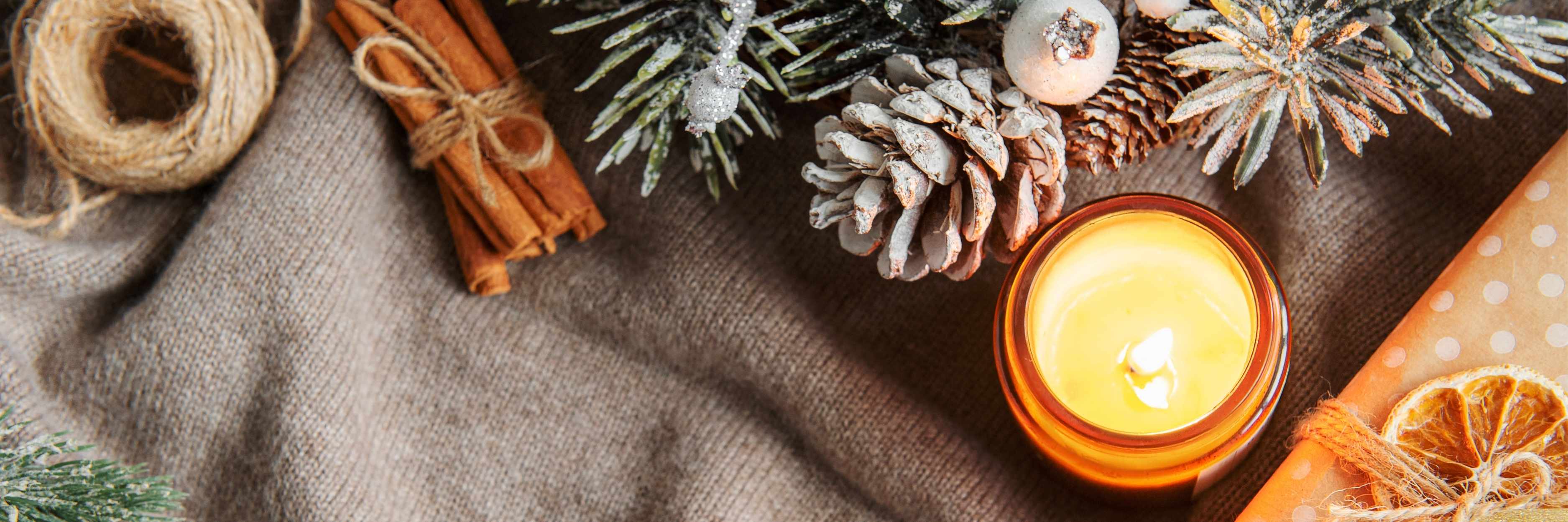 Candle with cinnamon sticks, pine cones, and decorative elements on a textured surface