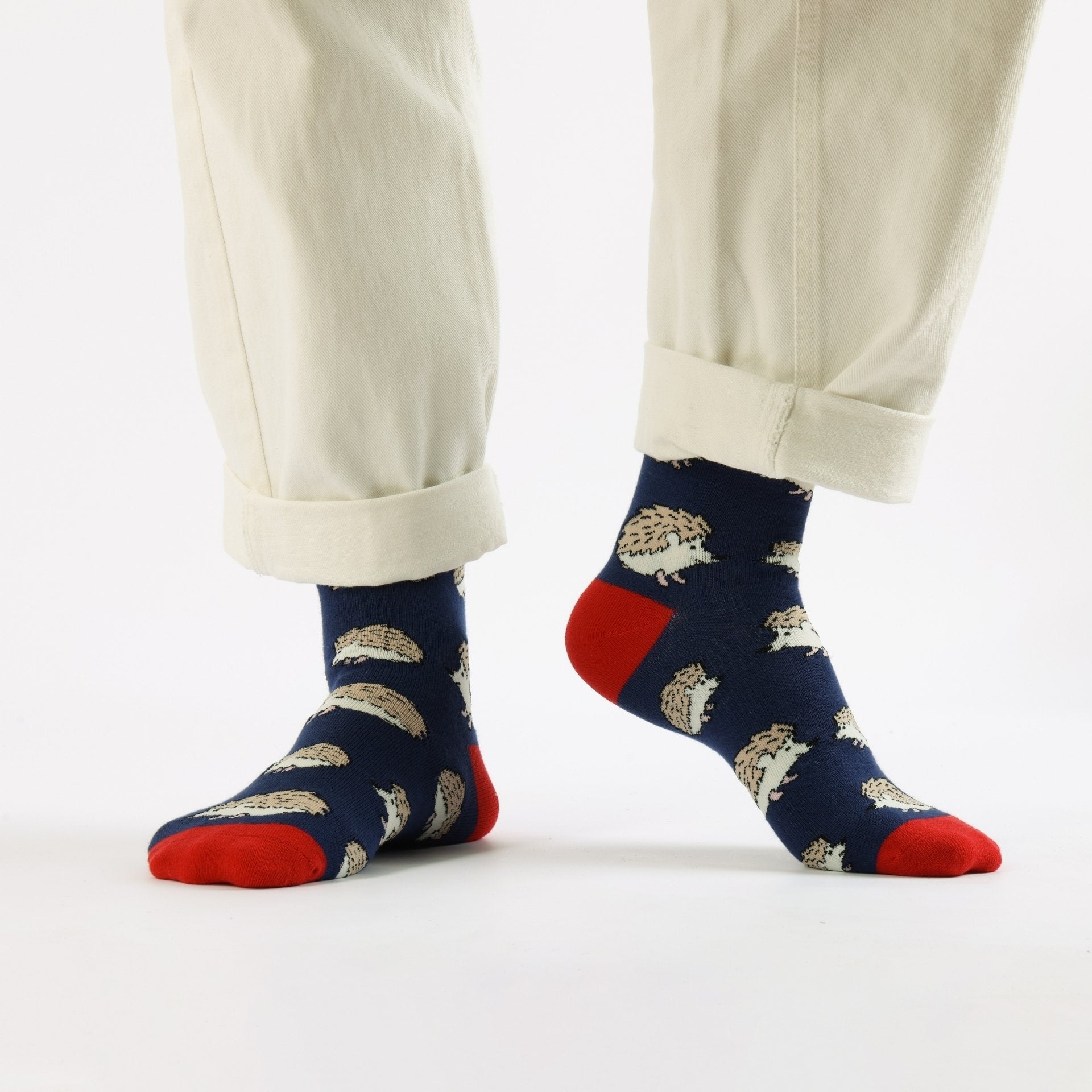 Navy socks with hedgehog pattern and red toes worn with beige pants on a white background