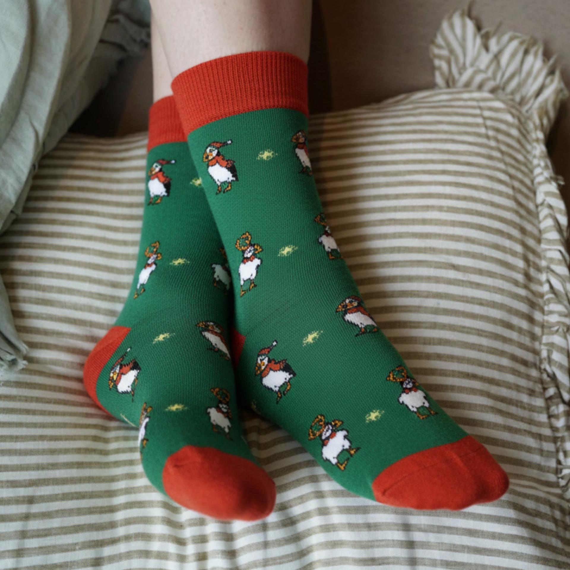 Green socks with puffin pattern and red accents worn on a striped bed.