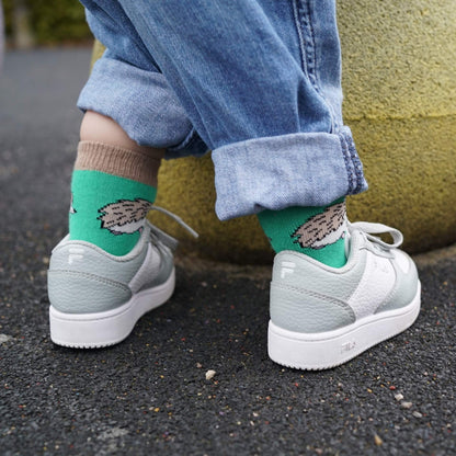 Kid wearing green socks with hedgehog print and white sneakers on a pavement.