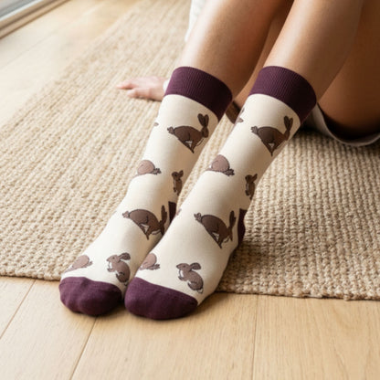 White socks with brown hare pattern and purple toes and cuffs worn by a person sitting on a wooden floor.