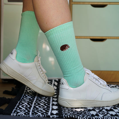 Model wearing a minimalist flat lay picture of pastel green ribbed socks with hedgehog motif design