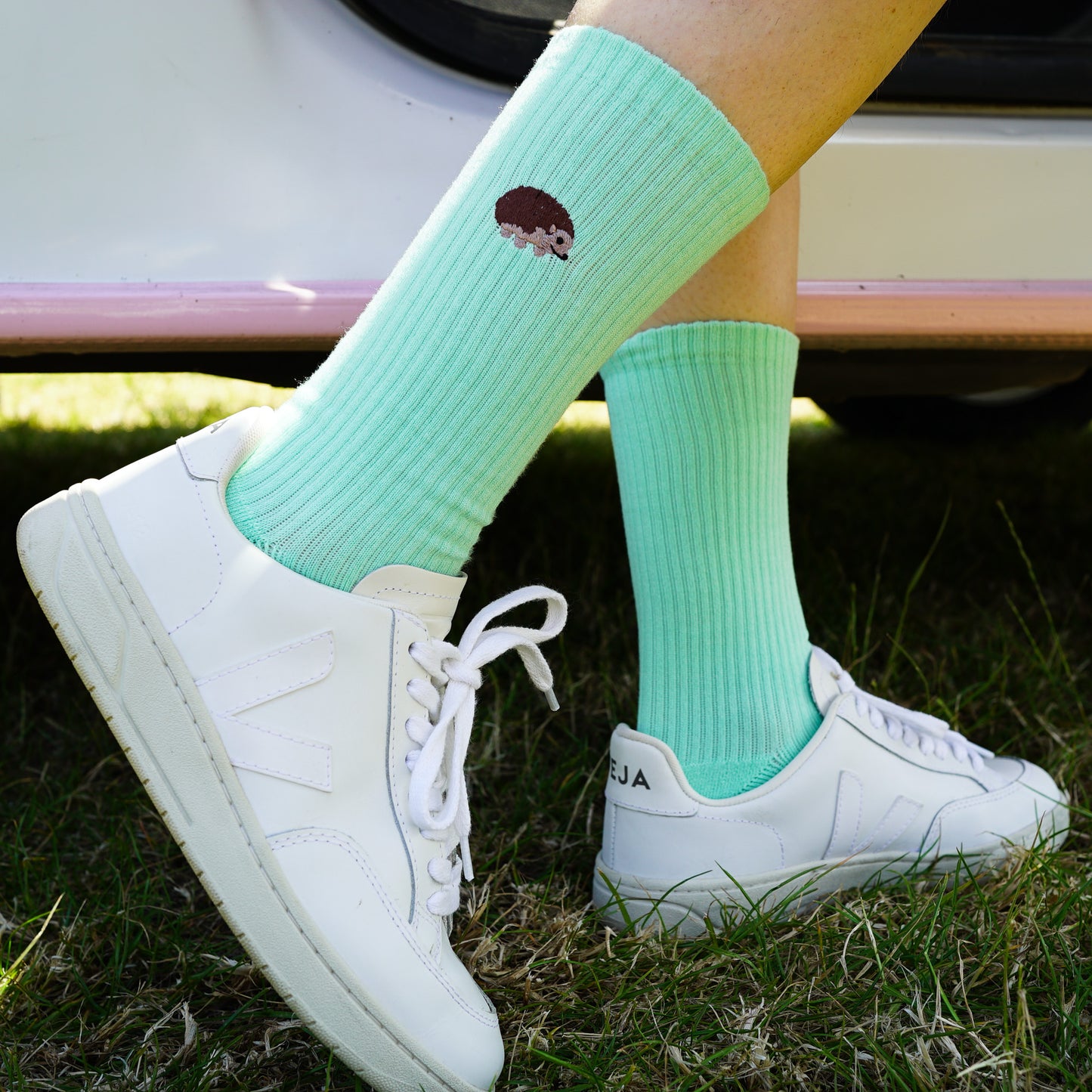 Model wearing a minimalist flat lay picture of pastel green ribbed socks with hedgehog motif design