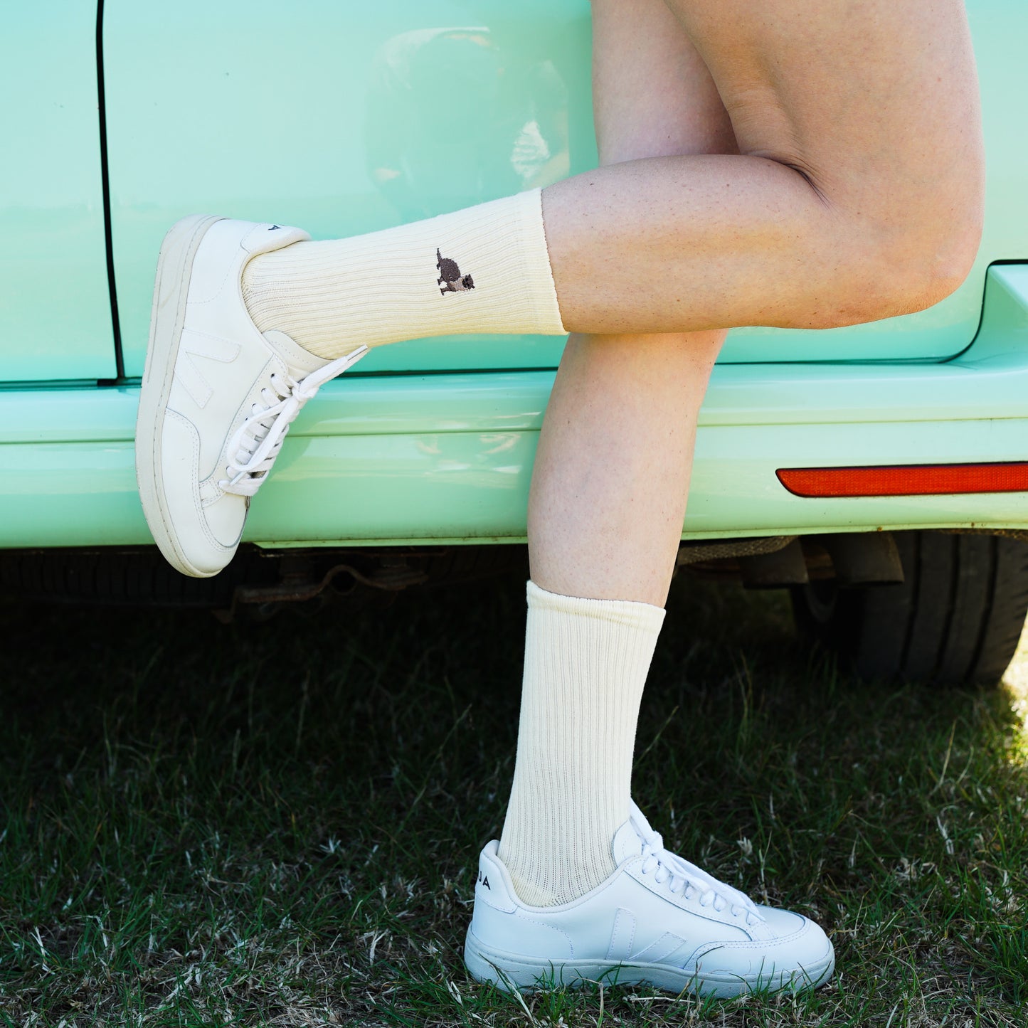 Model wearing pastel yellow ribbed bamboo socks with embroidered otter motif on the cuf