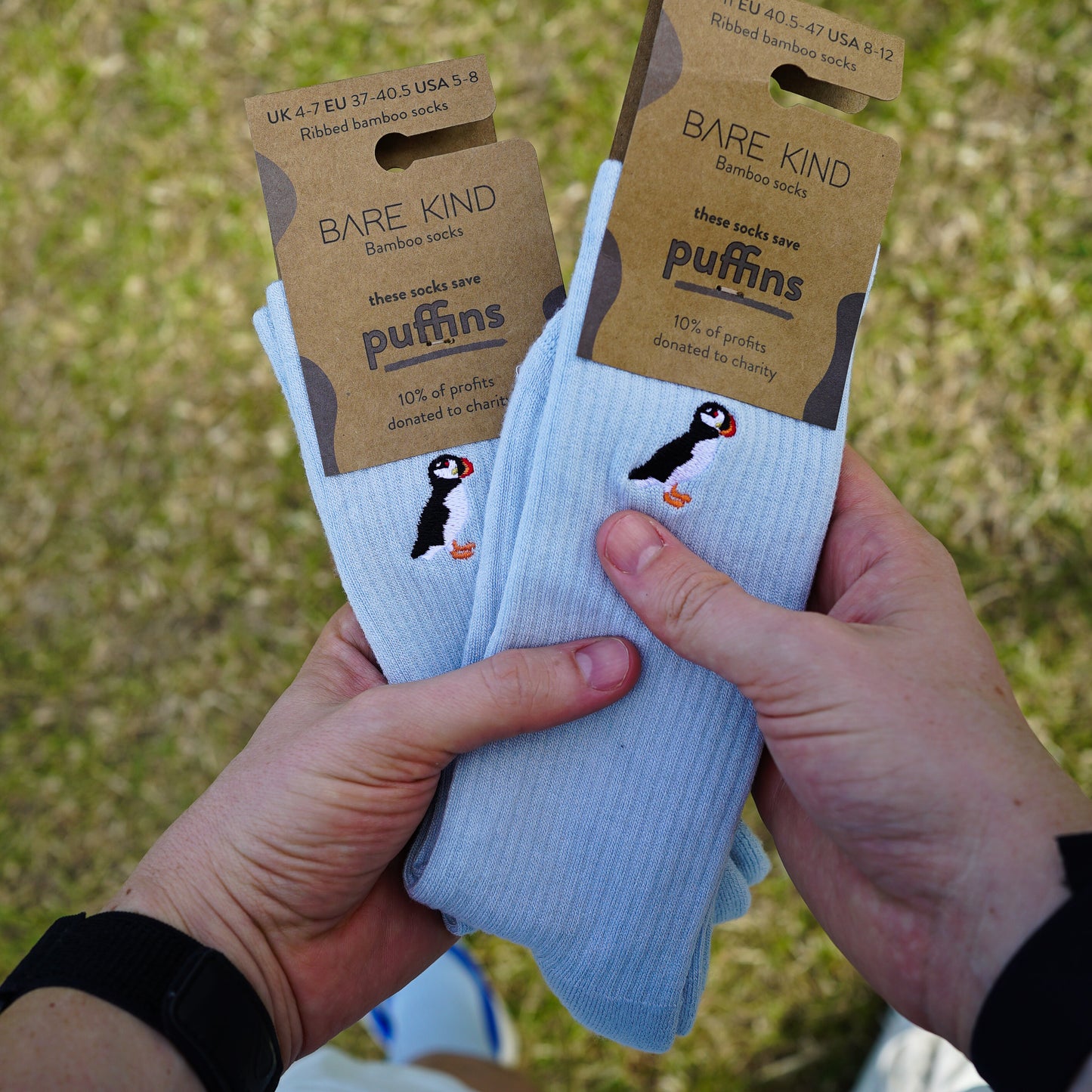 Model holding two packagings picture of blue ribbed bamboo socks with puffin embroidered design on cuff