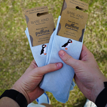 Model holding two packagings picture of blue ribbed bamboo socks with puffin embroidered design on cuff