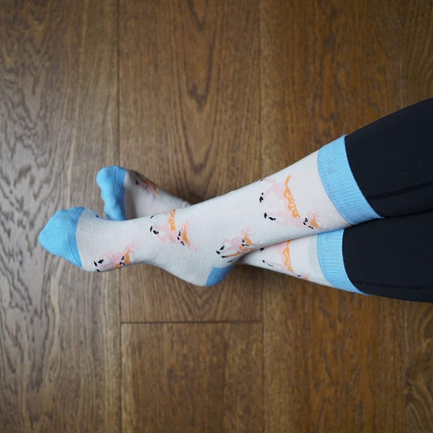 Person wearing deer socks sitting on a couch with wooden floor.