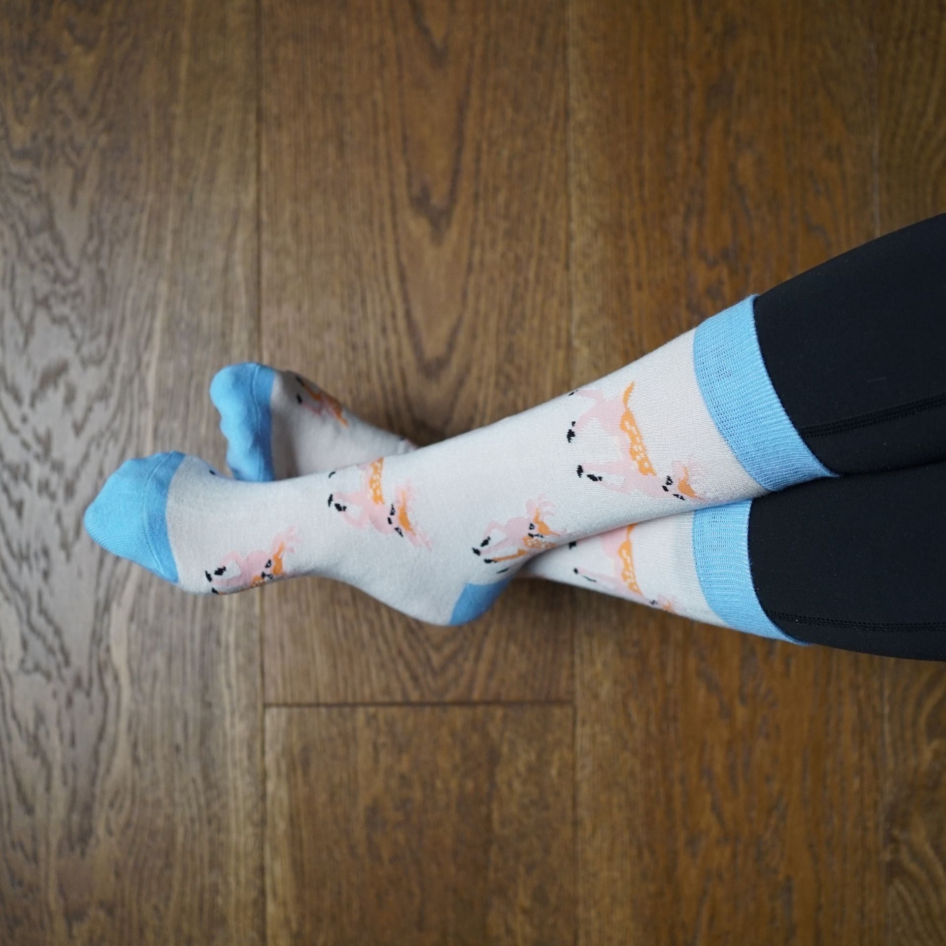 Person wearing deer socks sitting on a couch with wooden floor.