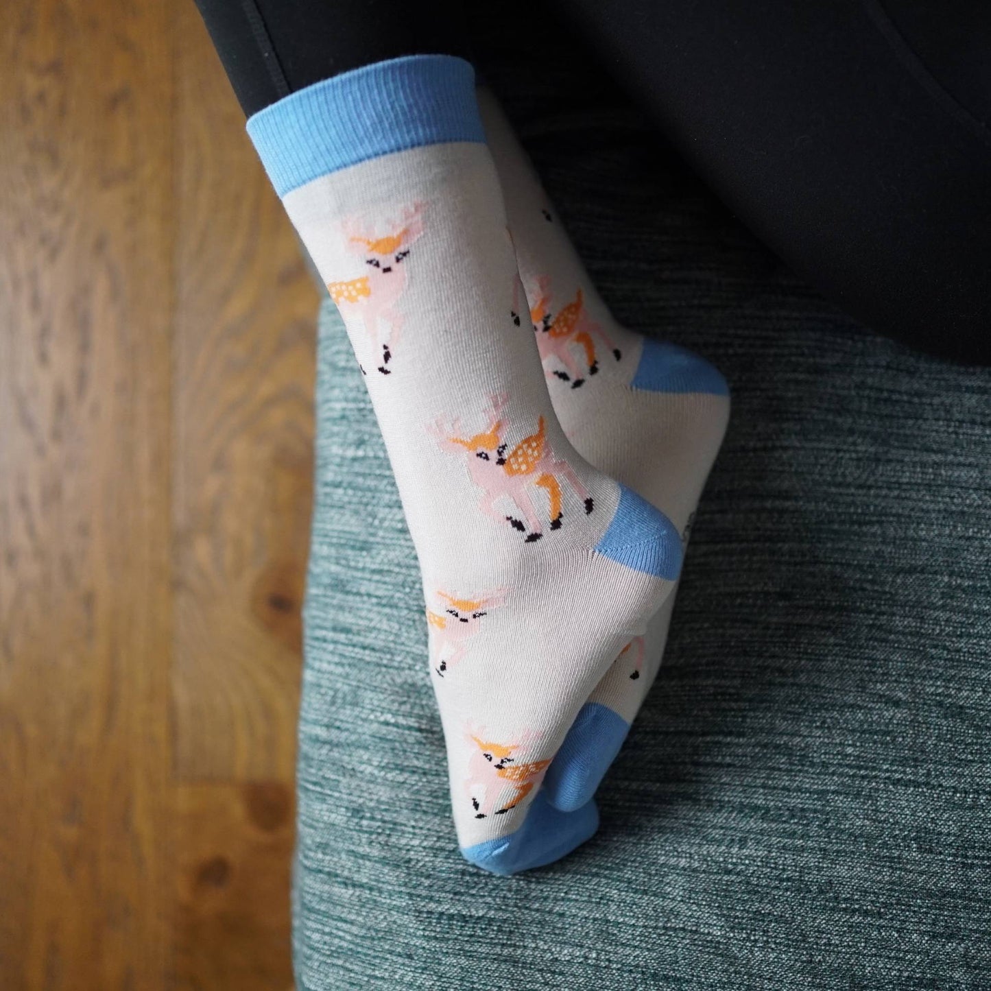 Person wearing deer socks sitting on a couch with wooden floor.