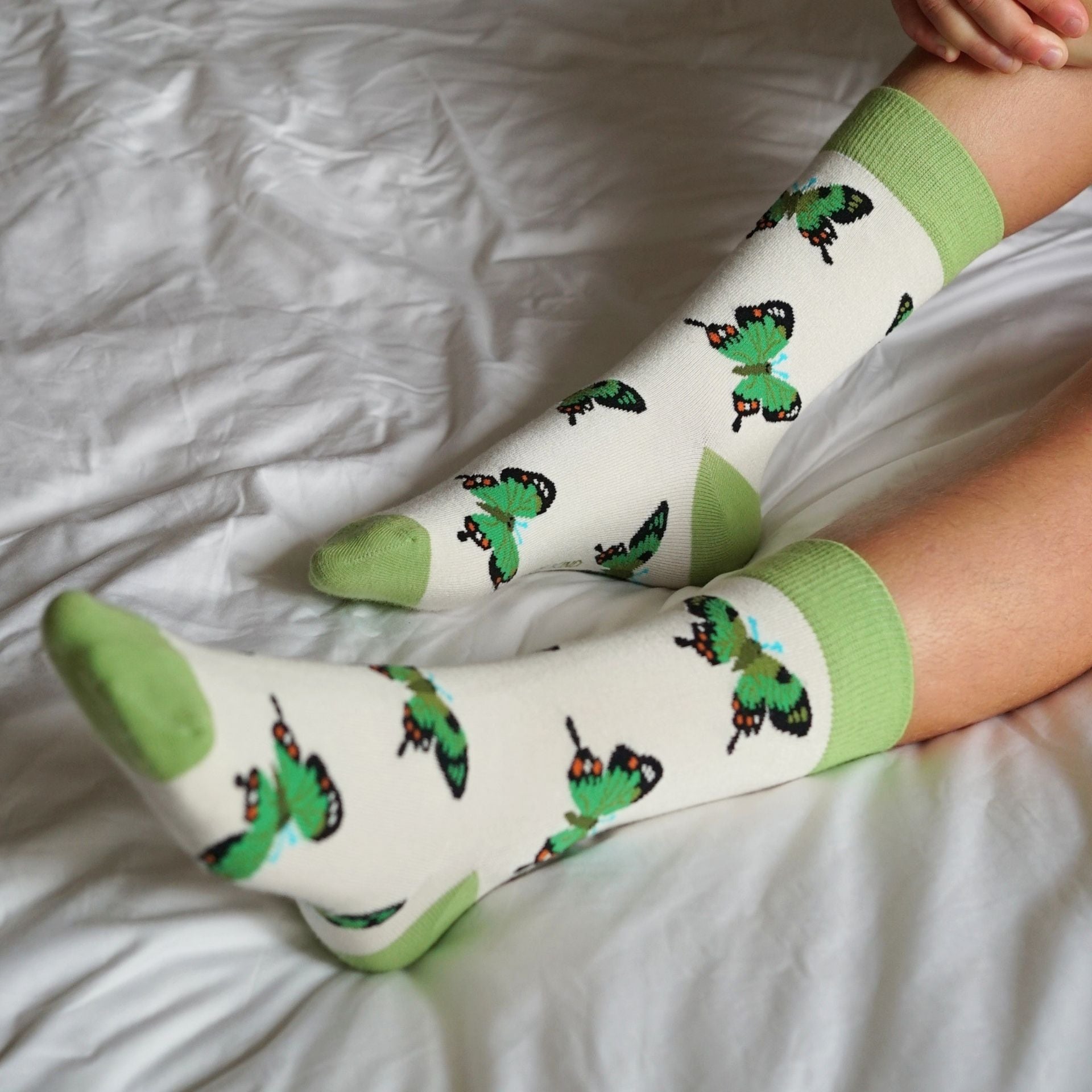 Person wearing socks with green and black designs on a white bed.