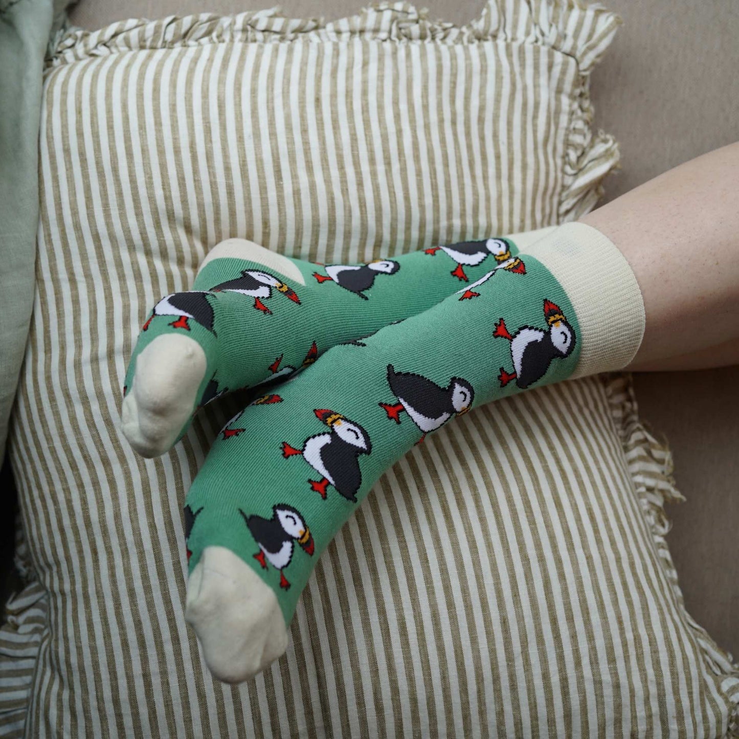Person wearing green socks with puffin design on a striped cushion