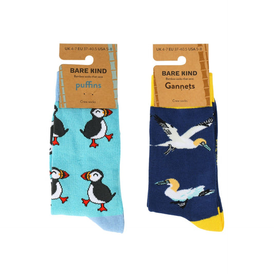 A pair of Bare Kind bamboo socks shown in two colors: one light blue with puffin prints and one navy blue with gannet prints. Both are on their original cardboard hangers against a white background.