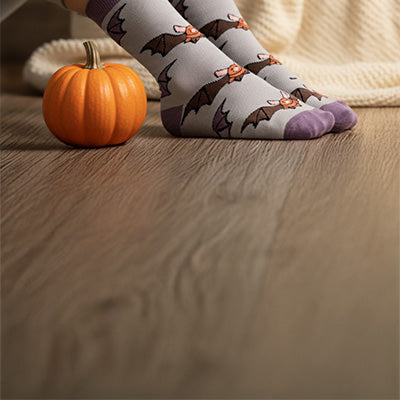 Person wearing bat socks with a small pumpkin on a wooden floor.