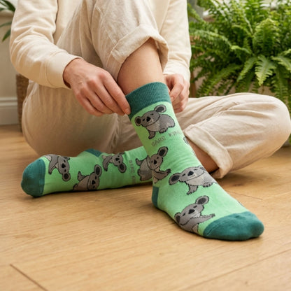 Person wearing green socks with koala designs on a wooden floor.