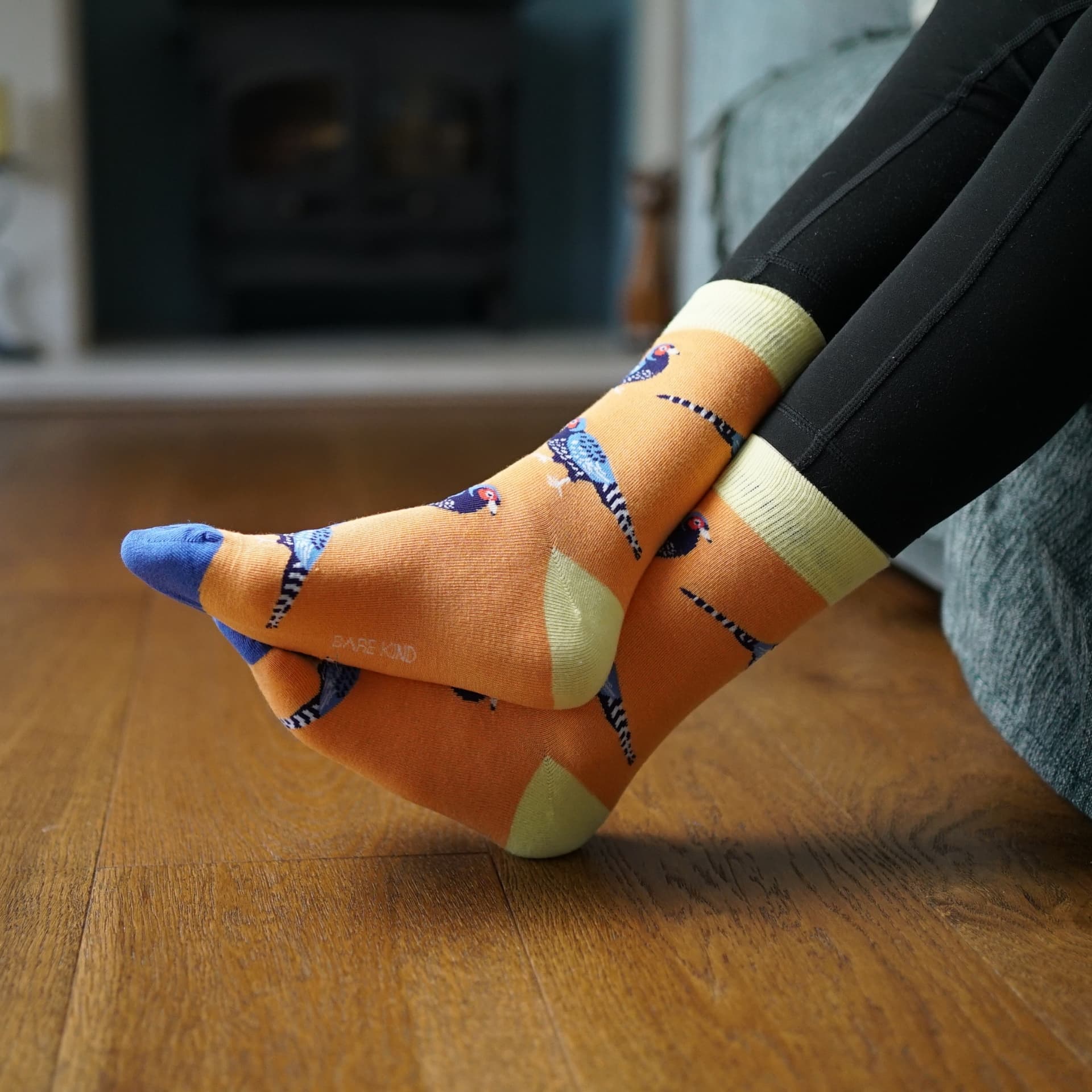 Person wearing orange socks with Pheasant design sitting on a couch.