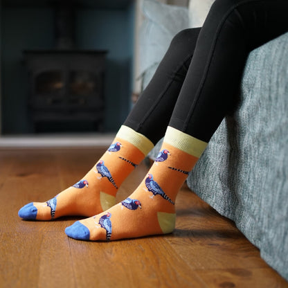Person wearing orange socks with Pheasant design sitting on a couch.