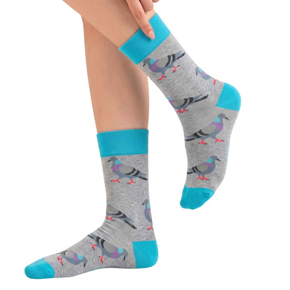 A pair of gray crew socks with a repeating pigeon pattern and bright turquoise accents, shown on a person's feet against a plain white background.