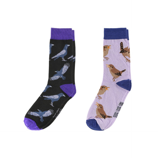 Two pairs of novelty crew socks shown side by side on a plain white background. The left sock is black with purple cuffs, heels, and toes, and features blue-gray bird illustrations.