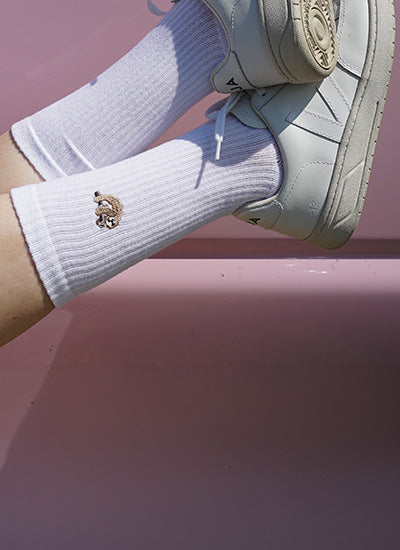 White socks with a sloth worn with light-colored sneakers on a pink background