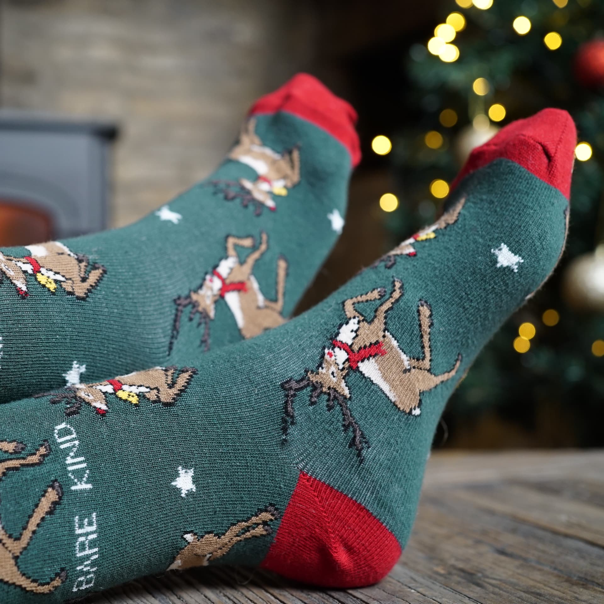 lifestyle image of model wearing green christmas reindeer bamboo socks in front of a christmas tree