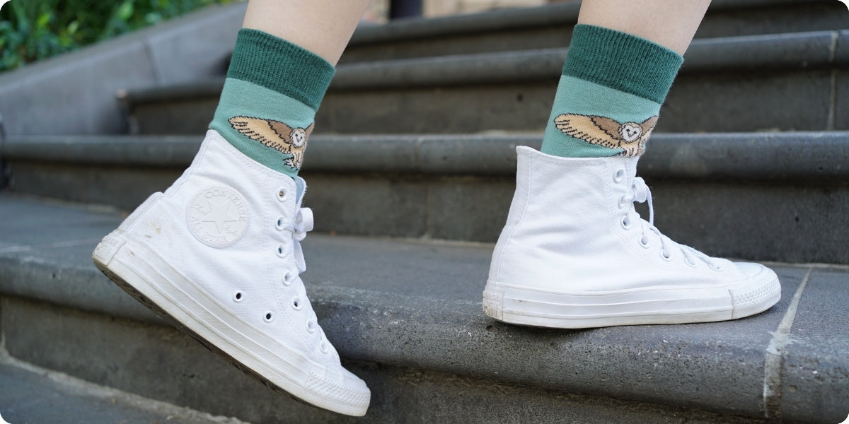 White high-top sneakers with green barn owl bamboo socks on a stone staircase.