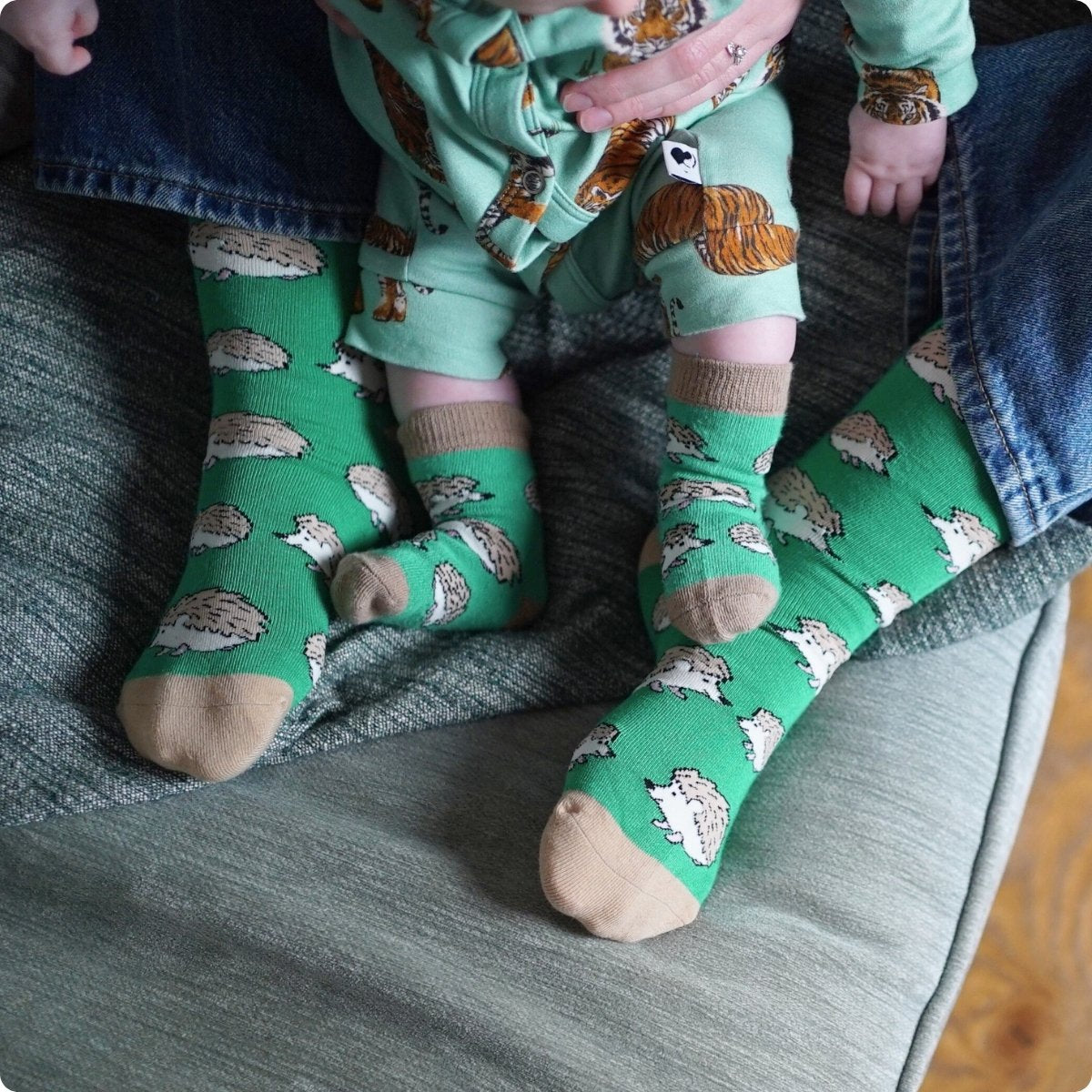 Child wearing green socks with hedgehog pattern sitting on a couch.