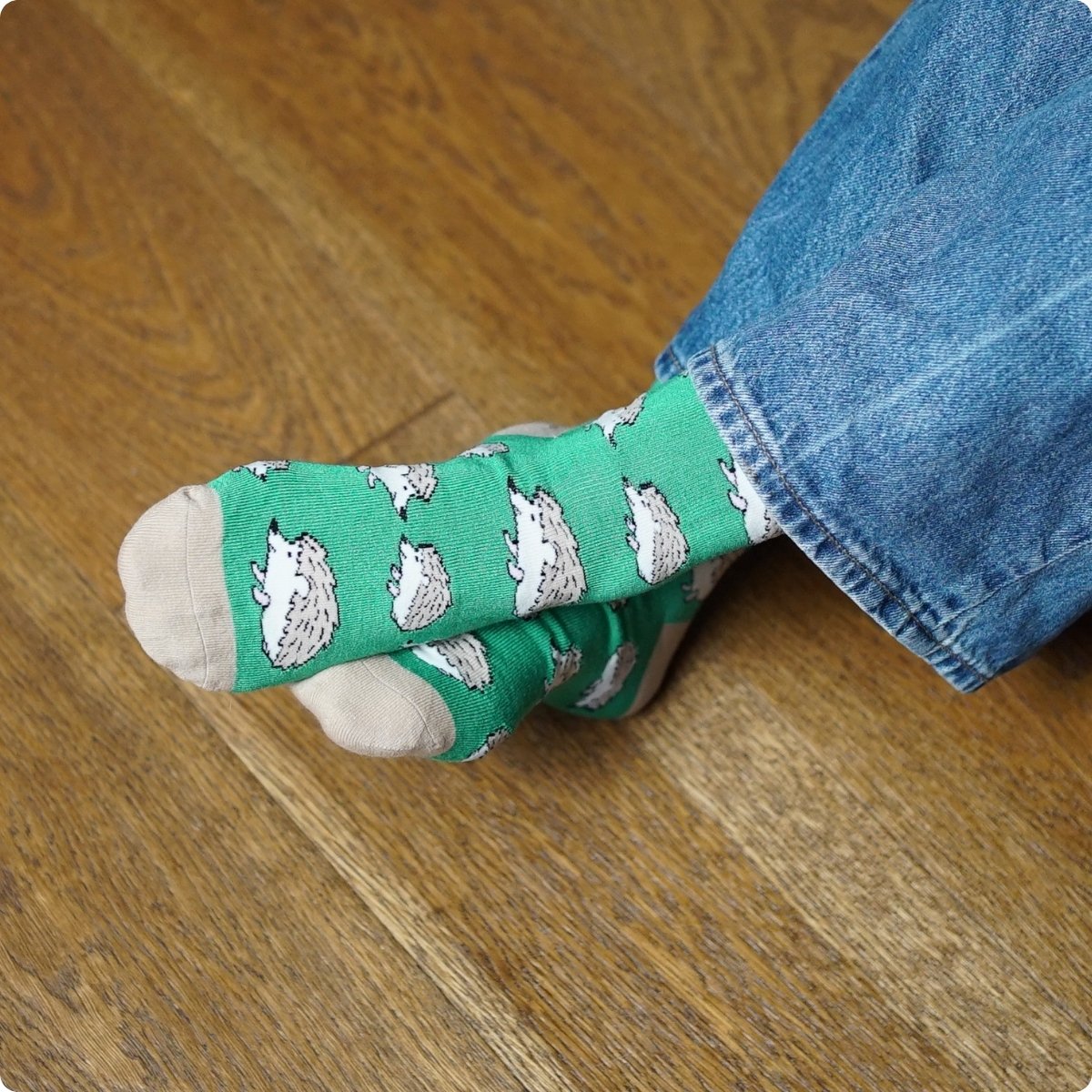 Green socks with hedgehog pattern worn by a person on a wooden floor