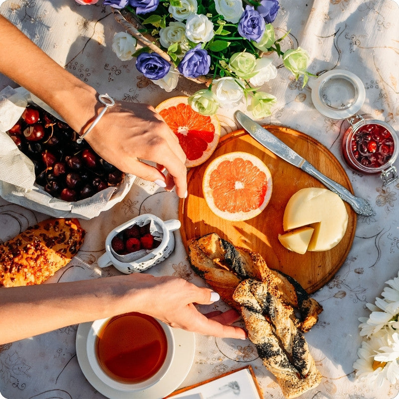 Person reaching for a grapefruit slice at a picnic table with various food items and flowers.
