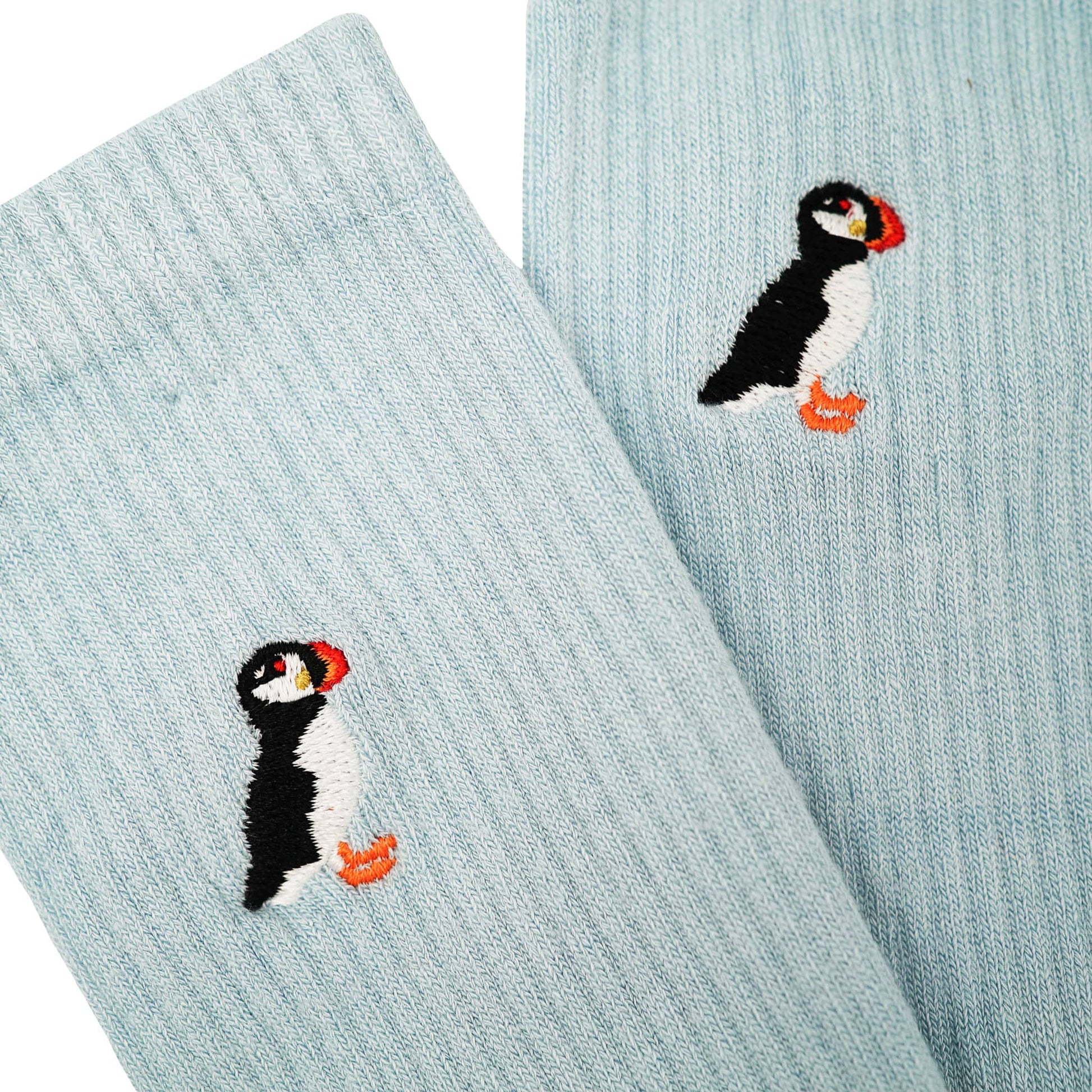 Close up to minimalist flat lay picture of blue ribbed bamboo socks with puffin embroidered design on cuff